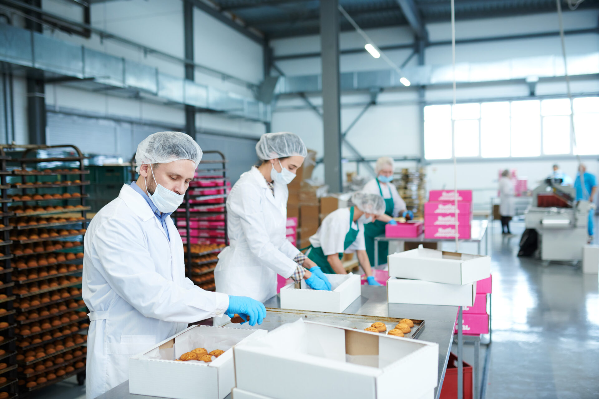 Confectionery factory workers in white coats collecting freshly baked pastry into paper boxes.